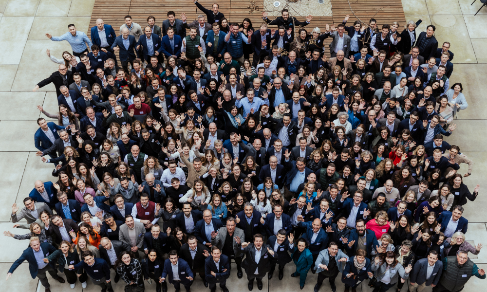 Sehr große Menschengruppe in Business-Kleidung schaut für ein Gruppenfoto nach oben in die Kamera.