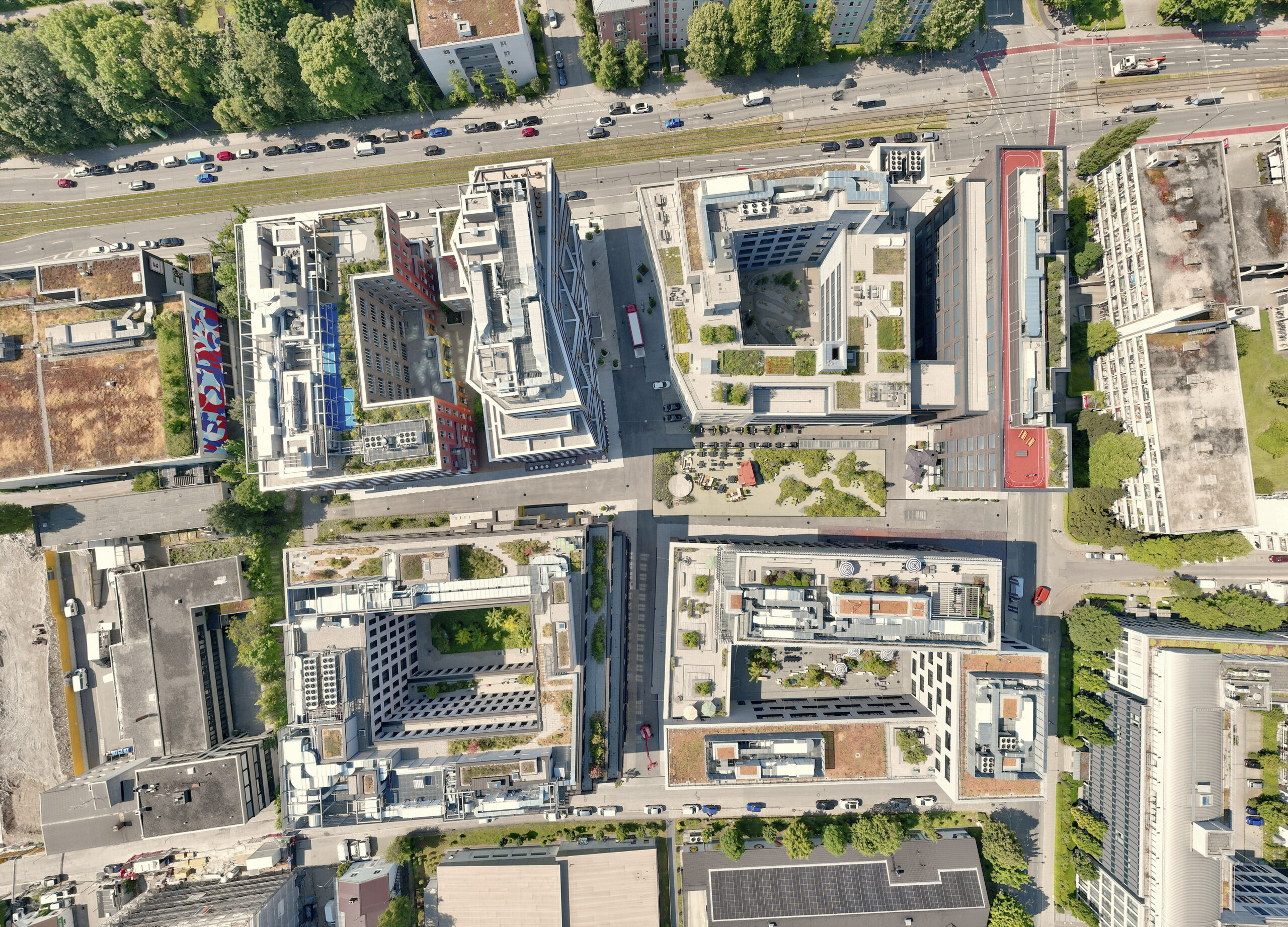 Luftaufnahme eines Stadtviertels mit mehreren modernen Gebäudekomplexen, Straßen und begrünten Dächern.