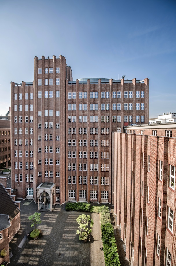 hohes Backsteingebäude im expressionistischen Stil mit vielen Fenstern und einem begrünten Innenhof.