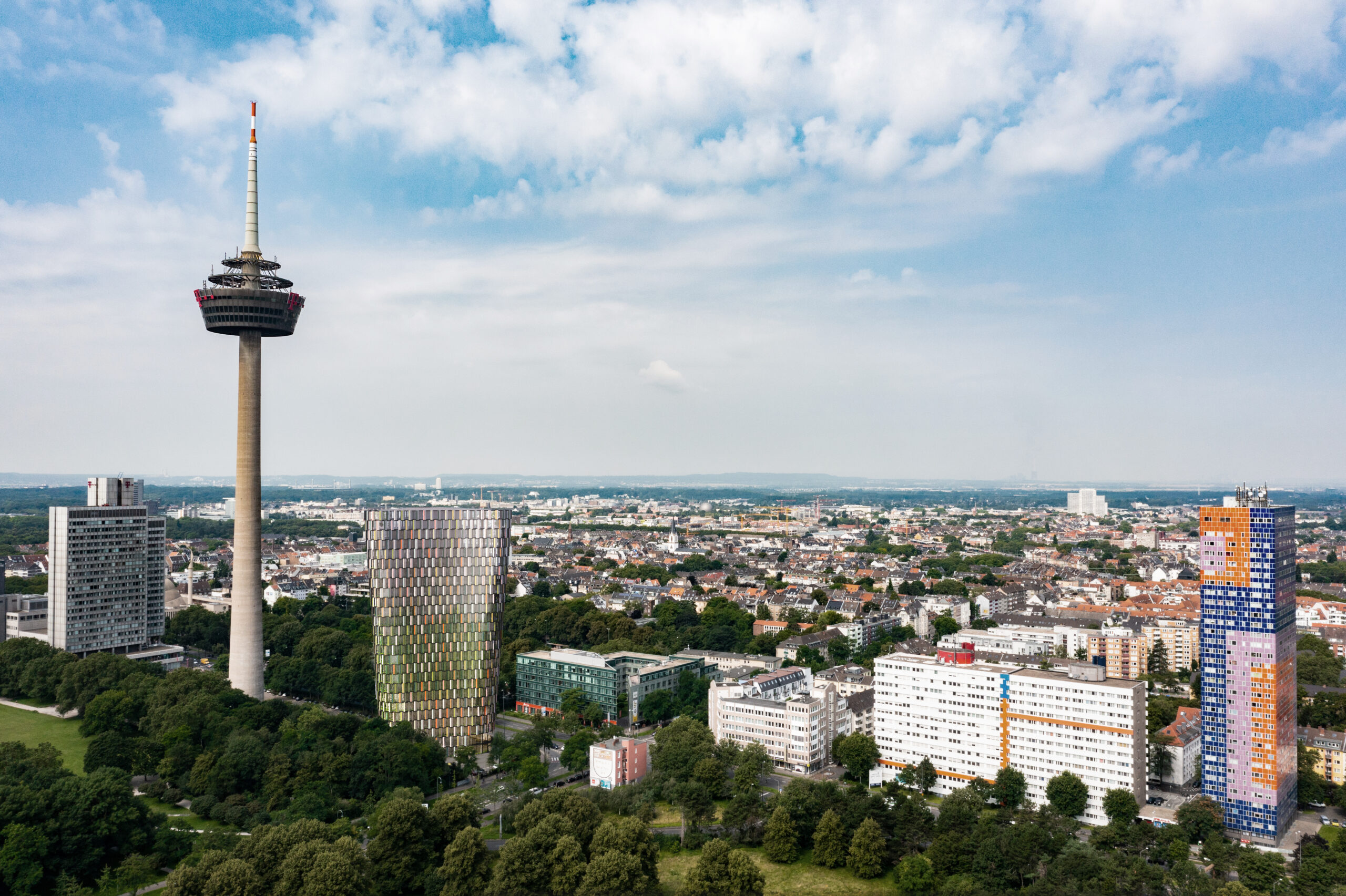 Stadtpanorama mit markantem Fernsehturm, Hochhäusern und teils grüner Umgebung.