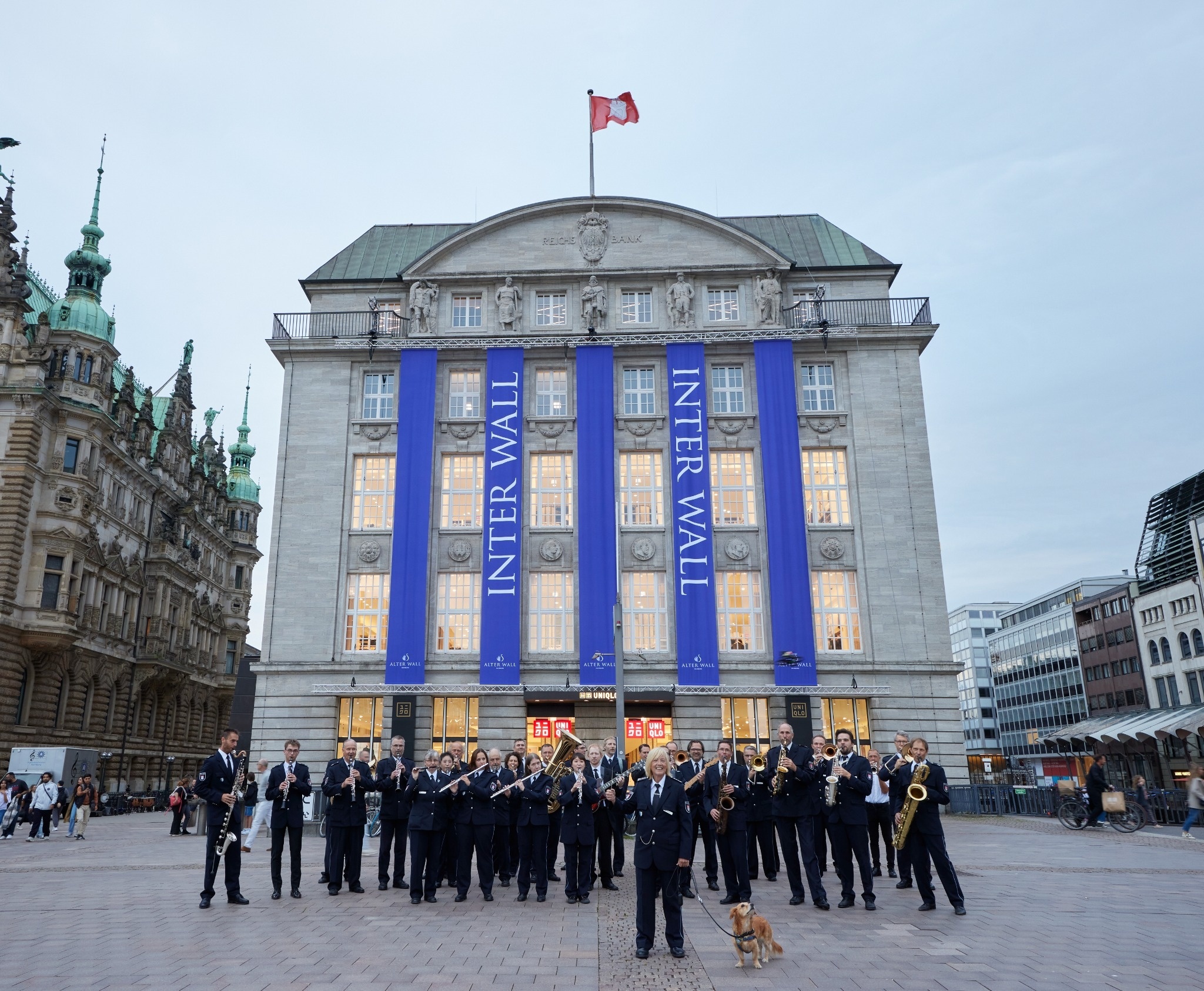 Historische Gebäude-Fassade mit der Aufschrift ‚Reichsbank‘, Statuen, blauen Bannern und Kupferturm im Hintergrund.
